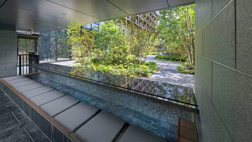 A modern indoor space with a glass barrier, a tiled floor, and a view of a landscaped garden.