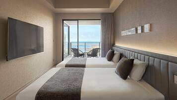 Quarto de hotel com duas camas, televisão, varanda com vista e mesa com cadeiras.