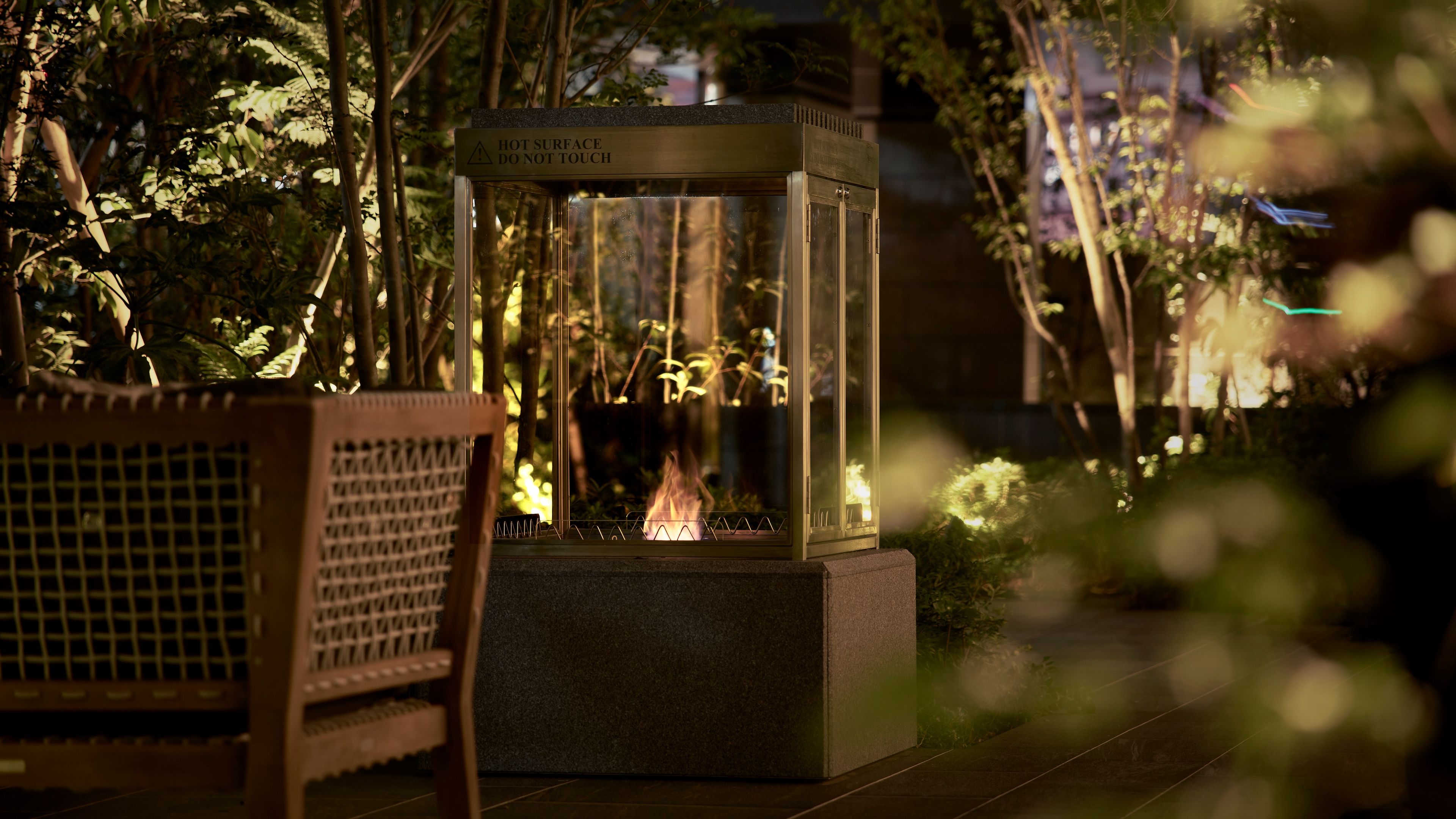 A glass enclosure with a warning sign, a fire inside, and a bench in the foreground.