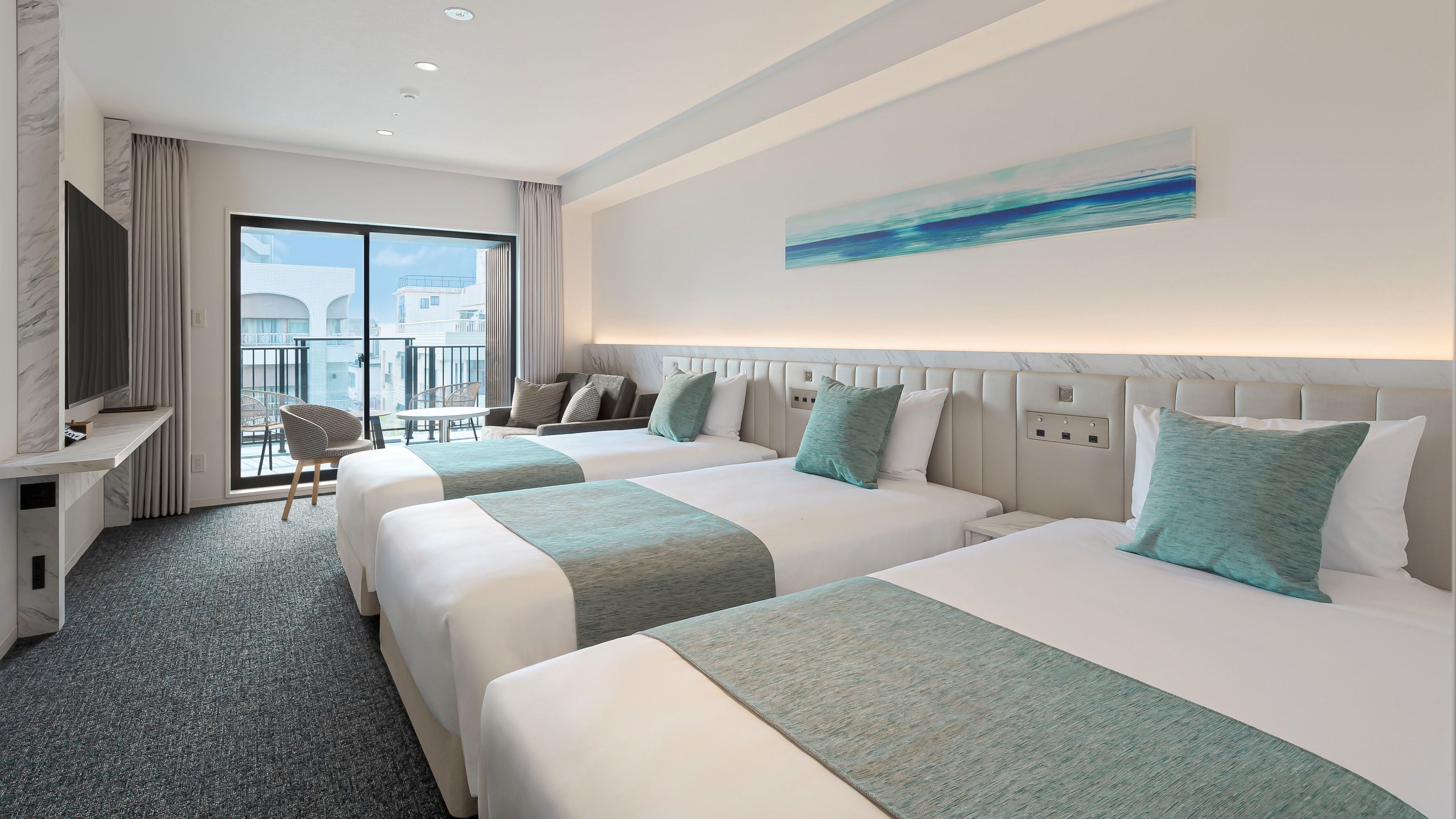A hotel room with two beds, a desk, a chair, and a balcony with a view.