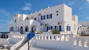 Un edificio blanco con contraventanas azules, una escalera y cielo azul despejado.