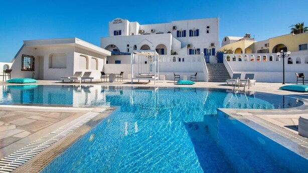 Una piscina con sillones de descanso y un edificio con paredes blancas y detalles azules.