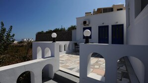 Un edificio blanco con puertas azules y un muro de piedra al fondo.