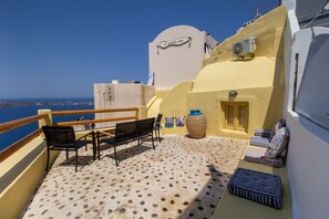 A balcony with a view of the sea, featuring a wooden railing, two black chairs, a large vase, and a small table. - Villa Ariadni (Santorini)