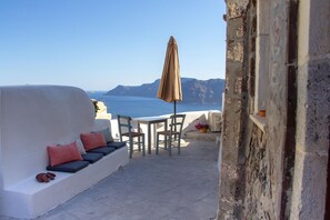 A terrace with a white wall, a table with chairs, and a view of the sea. - Villa Ariadni (Santorini)