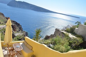 A balcony with a view of the sea, a table, chairs, and a yellow umbrella. - Villa Ariadni (Santorini)