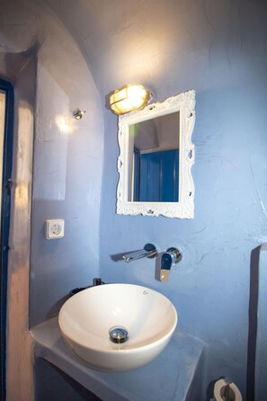 A bathroom with a white sink, a mirror with an ornate frame, and a light fixture above the mirror. - Villa Ariadni (Santorini)