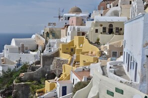 A coastal village with white-washed buildings, a prominent yellow structure, and a sign for 'Caldera Massages Studio'. - Villa Ariadni (Santorini)