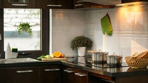 A modern kitchen with dark wood cabinets, a stainless steel countertop, a hanging plant, a potted plant, and a window with a view. - Poonsa Duy Tan (Hanoi)