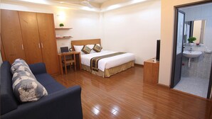 A hotel room with a bed, a desk with a laptop, a wardrobe, a sofa, and a bathroom with a sink and mirror. - Poonsa Duy Tan (Hanoi)