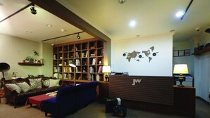A reception area with a wooden reception desk, a world map on the wall, a bookshelf filled with books, a blue sofa, and a brown leather couch. - Jinwoo Residence (Geoje)