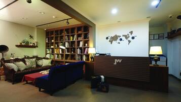 A reception area with a wooden reception desk, a world map on the wall, a bookshelf filled with books, a blue sofa, and a brown leather couch.