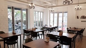 A spacious dining area with multiple tables and chairs, large windows, and hanging chandeliers. - Jinwoo Residence (Geoje)