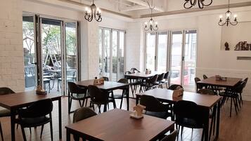 A spacious dining area with multiple tables and chairs, large windows, and hanging chandeliers.