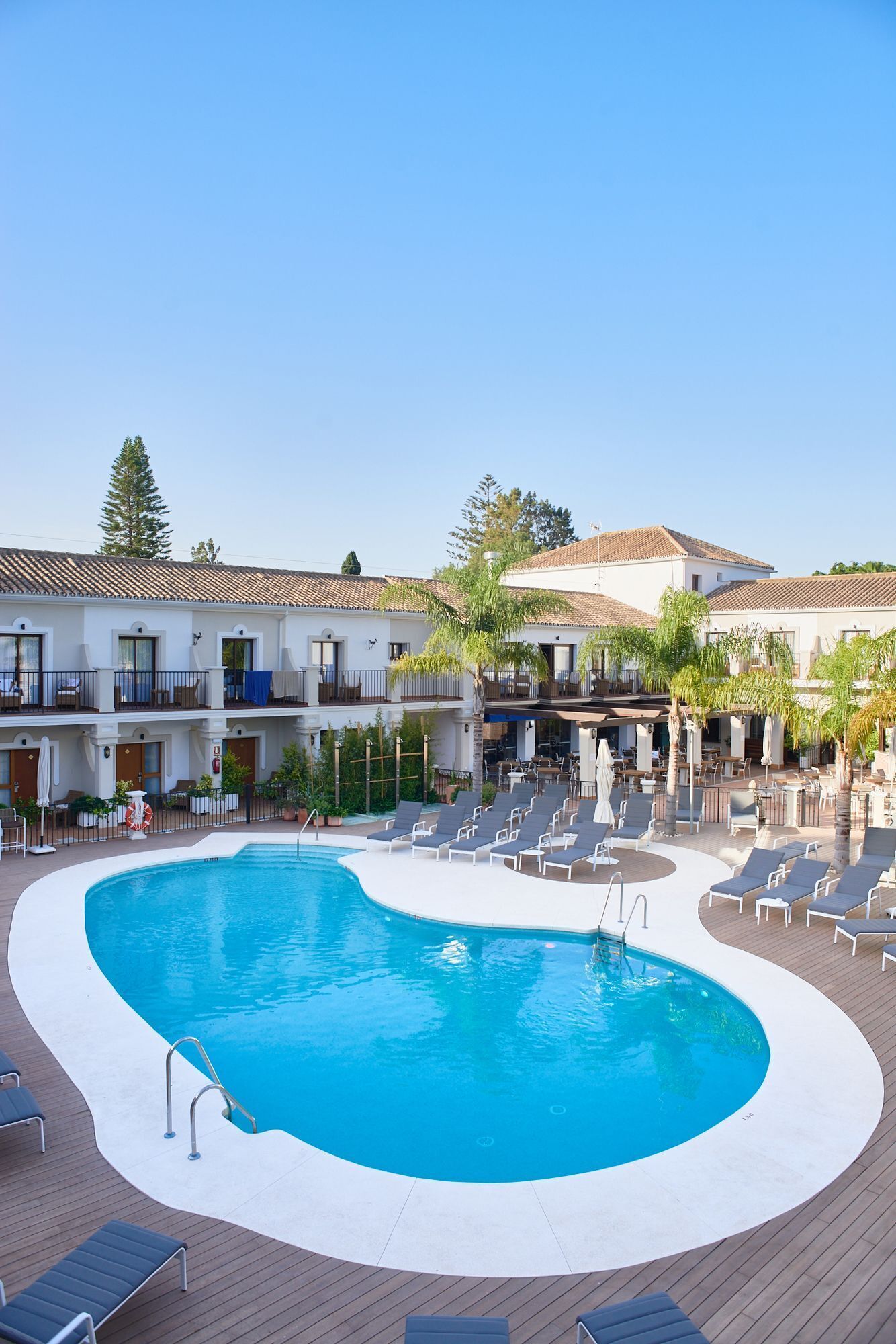 A swimming pool with lounge chairs and a covered area, surrounded by buildings with balconies and outdoor seating.