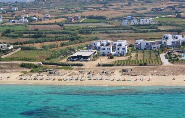 Una zona costanera amb edificis blancs, una platja de sorra amb sombreretes i una vista clara del mar.