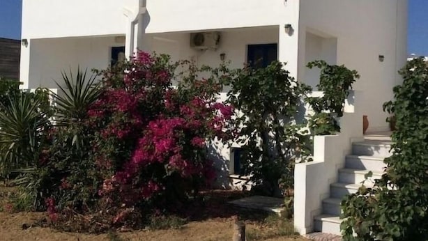 A white two-story building with a blue sign on the top left. - Aronis (Naxos)