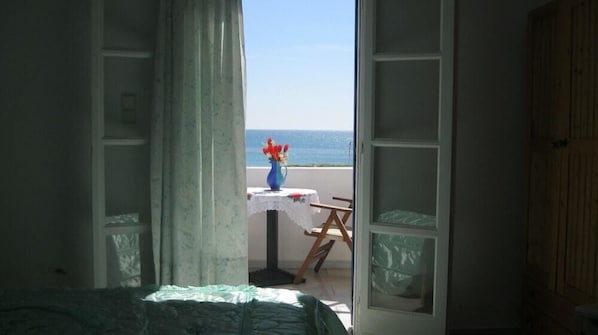 A room with a bed, a table with a vase, and a view of the sea through an open door. - Aronis (Naxos)