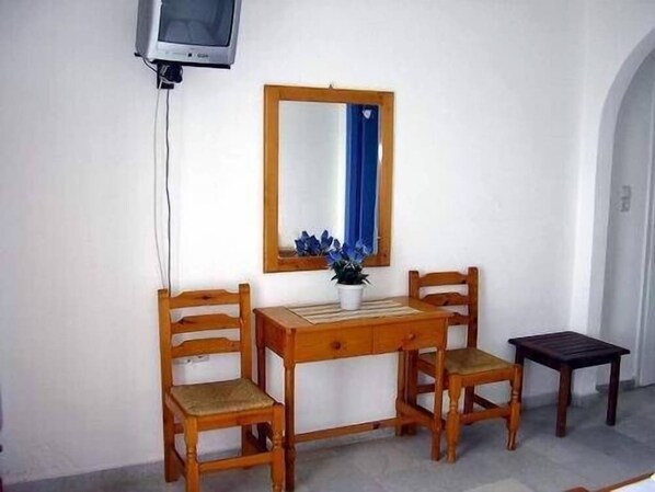 Une petite pièce avec un bureau en bois, deux chaises, un miroir et un téléviseur.