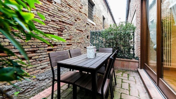 A brick building with a wooden table and chairs in a courtyard. - Bluesky (Venice)