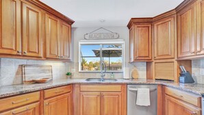 A kitchen with wooden cabinets, a granite countertop, a sink, and a sign that reads "Beach House". - Siesta Key Pool House (Siesta Key)