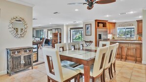 A spacious dining area with a glass-top table and multiple chairs, a ceiling fan, and wooden cabinetry. - Siesta Key Pool House (Siesta Key)