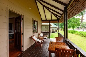 Um deck de madeira com mesa e cadeiras, uma área coberta com telhado e vista para um jardim exuberante.