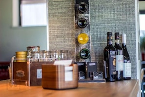 Una zona de bar con botellas de vino, copas y un refrigerador con la marca Coca-Cola.