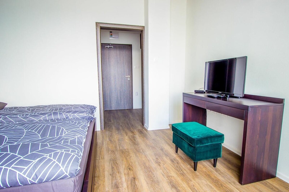 A hotel room with a bed, a desk with a television, and a door leading to another room.