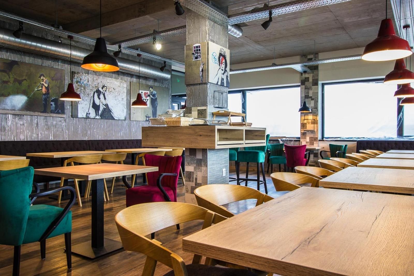 L’intérieur d’un restaurant est décoré de tables et de chaises en bois, d’un éclairage suspendu rouge et d’une fresque murale.