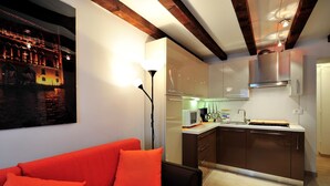 Une cuisine moderne avec un îlot central, un coin repas doté d’un canapé rouge et un tableau représentant un bâtiment accroché au mur.
