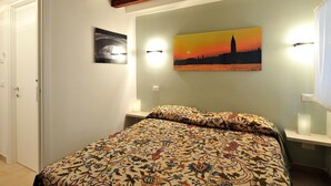 Une chambre à coucher avec un lit, un tableau représentant un coucher de soleil et une poutre en bois au plafond.