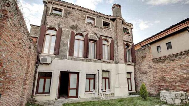 A two-story building with a courtyard, featuring a brick facade, arched windows, and a small garden area with a pathway leading to the entrance. - Venice Garden (Venice)