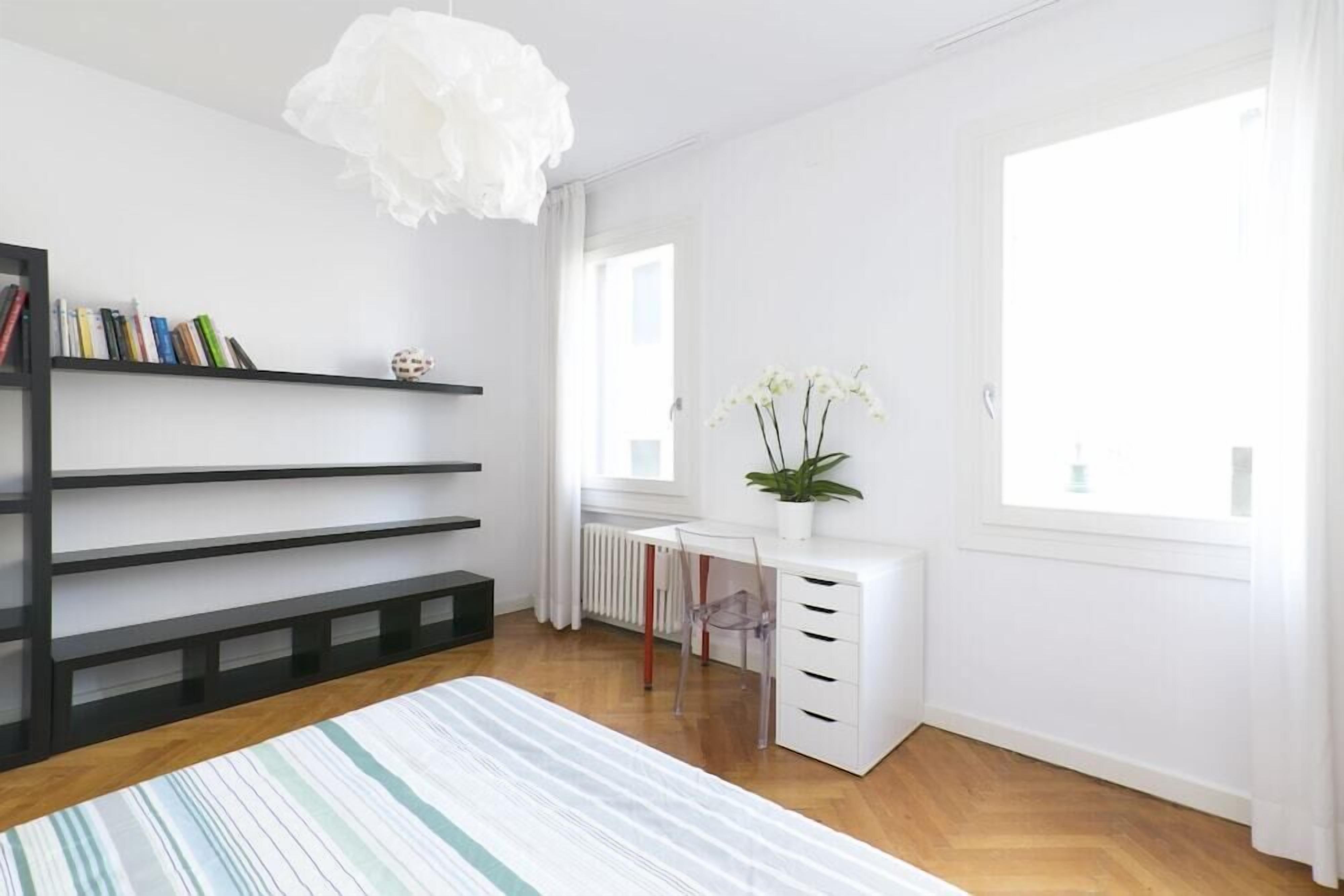 A modern bedroom with a bed, a desk, and a bookshelf.