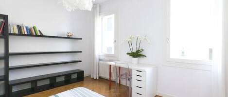 A modern bedroom with a bed, a desk, and a bookshelf.