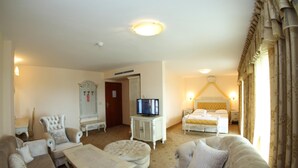 A hotel room with a large bed, a television on a cabinet, a sofa, a chair, and a small table. - Duni Royal Resort - Hotel Pelican (Sozopol)
