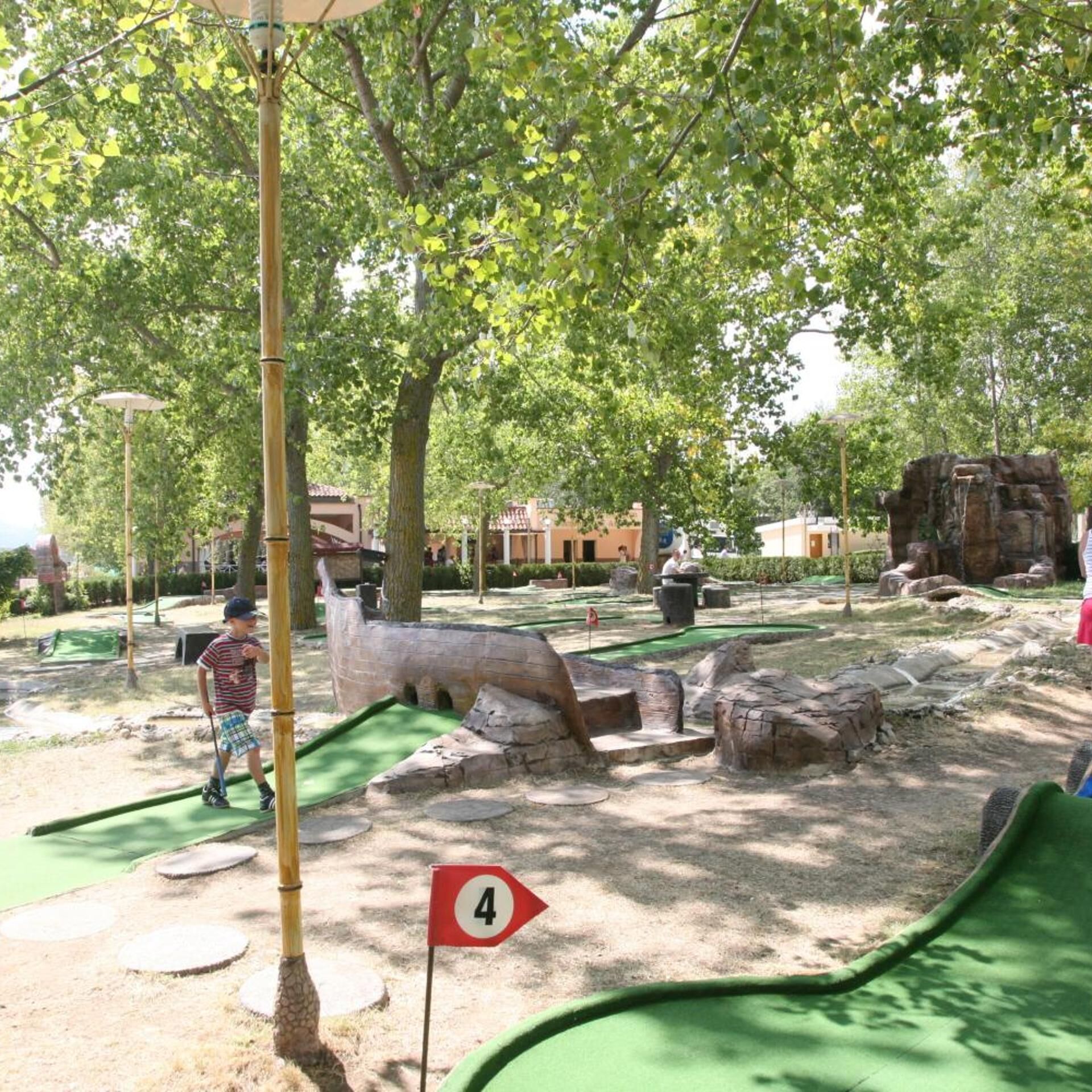 Un campo da minigolf con una zona verde per le putt, il buco numero 4 e alberi circostanti.