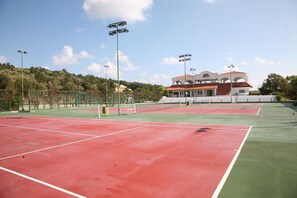 Canchas de tenis múltiples, un edificio con techo rojo y una cerca verde.
