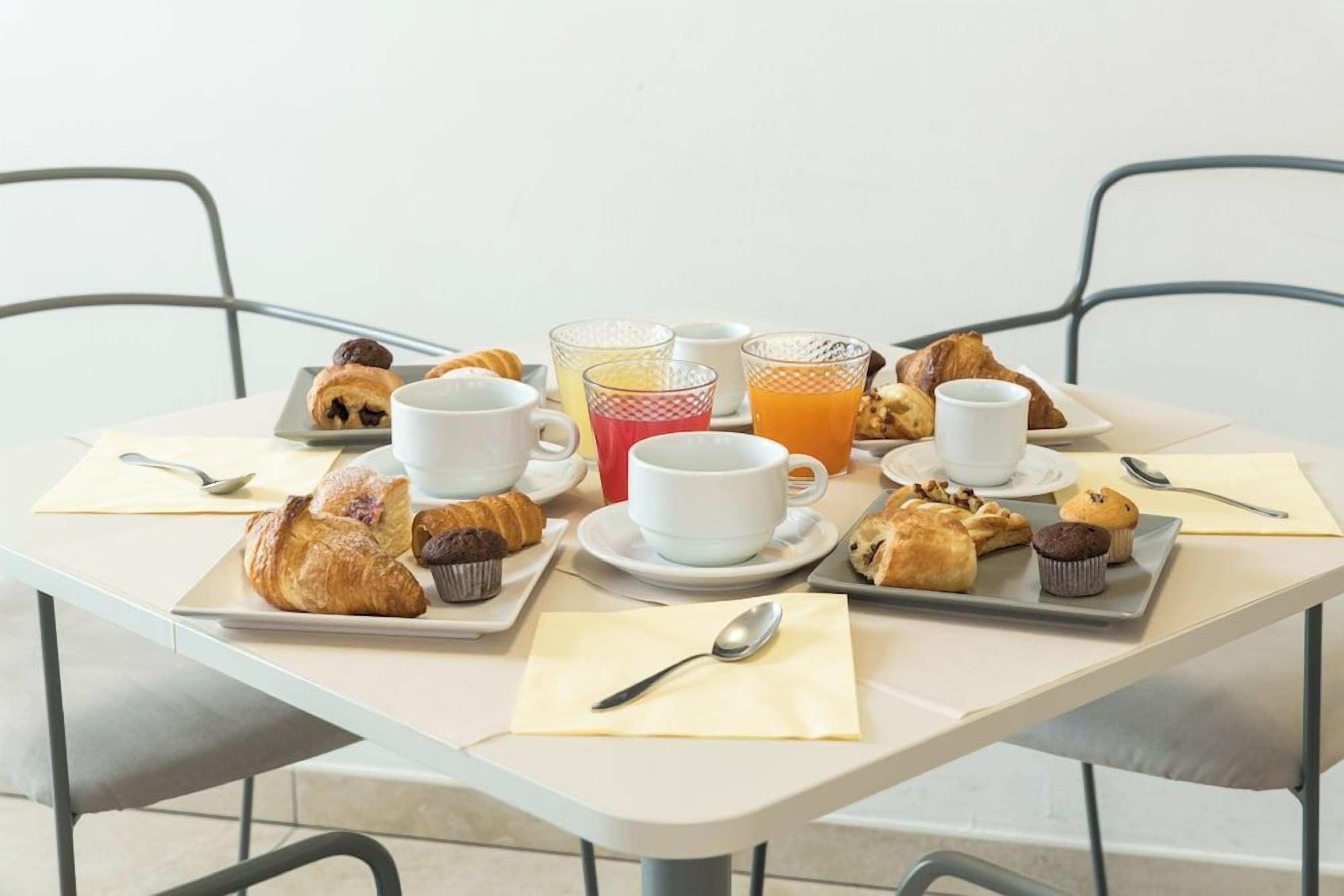 A breakfast setting with croissants, muffins, and juice on a table.