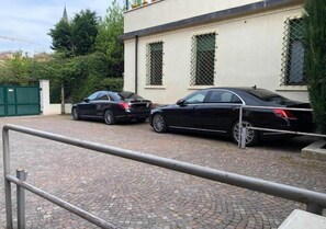 A paved driveway with two black cars parked in front of a building with barred windows. - STH Verona (Verona)