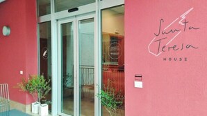 A building entrance with glass doors, a red wall, and a sign reading "Santa Teresa HOUSE". - STH Verona (Verona)