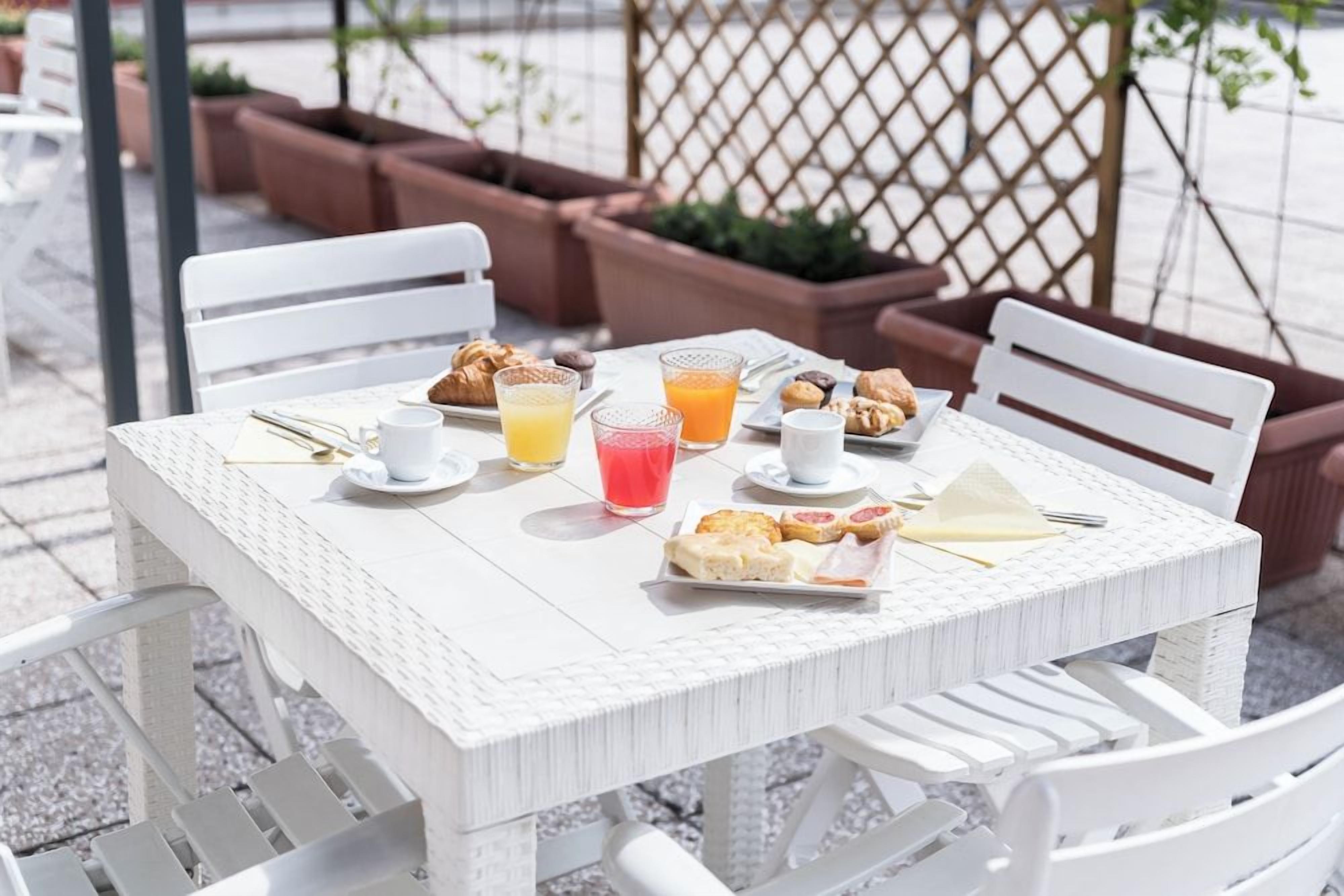 Une table en osier blanche, sur laquelle sont disposés des aliments pour le petit-déjeuner, notamment des croissants, du jus et des viennoiseries.