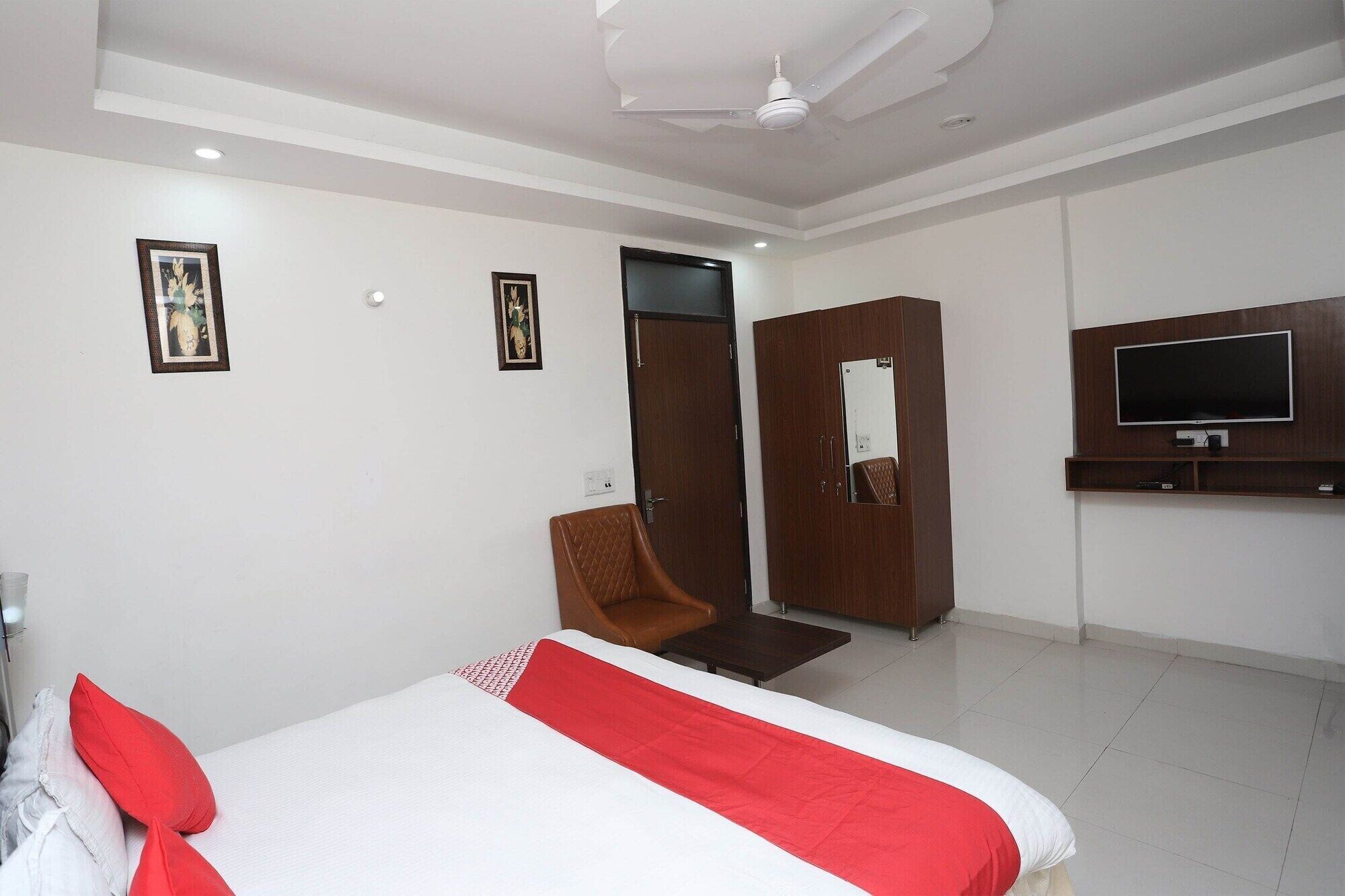 A hotel room with a bed, a TV mounted on the wall, a wardrobe, and a chair.