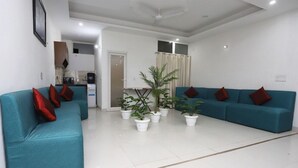 Ein modernes Wohnzimmer mit türkisfarbenen Sofas, roten Kissen und mehreren Topfpflanzen.