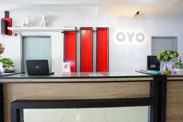 A reception desk with a laptop, a red door, and a sign that reads 'OYO.' - Prince Boulevard Hotel (Manado)