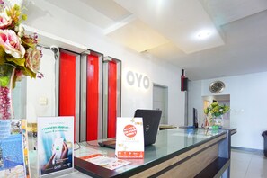 A reception desk with a glass partition, a laptop, a clock, and a sign promoting the OYO app. - Prince Boulevard Hotel (Manado)