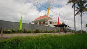 A two-story house with a red roof, surrounded by a low wall and a grassy area. - D Lobong Suite (Ubud)