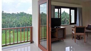 A balcony with a TV stand and seating, overlooking a lush green landscape. - D Lobong Suite (Ubud)