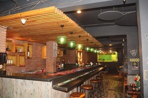 Zona de bar con una barra alargada, taburetes y lámparas colgantes verdes.