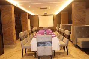 A conference room with a long table, chairs, a projector screen, and a carpeted floor. - Kyriad Hotel Indore by Othpl (Indore)